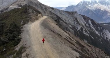 Kırmızı ceketli kadın dağlarda koşuyor.