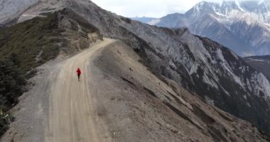 Kırmızı ceketli kadın dağlarda koşuyor.