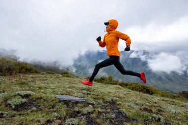 Yüksek irtifada dağ zirvesinde koşan kadın koşucu.