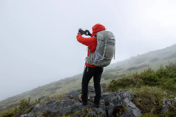 ハイキングの女性は 標高の高い山で写真を撮るスマートフォンを使用します — ストック写真