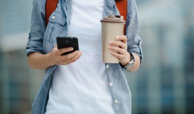 İnsanlar ellerinde kahve bardağıyla yürürken cep telefonu kullanıyor.