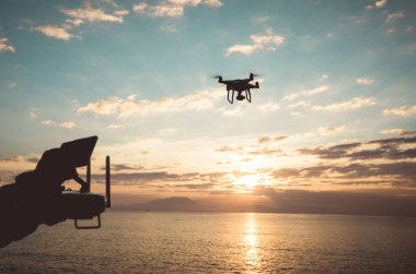 Uzaktan kumandalı siluet güneş doğarken deniz üzerinde fotoğraf çeken uçan bir dron. 