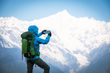 Sırt çantalı bir kadın akıllı telefonuyla yüksek irtifa dağlarının fotoğrafını çekiyor.