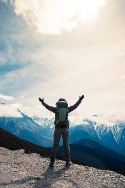 Kadın yürüyüşçü, dağın tepesindeki uçurumun keyfini çıkar. Tibet 'teki kar kaplı dağlara bak.