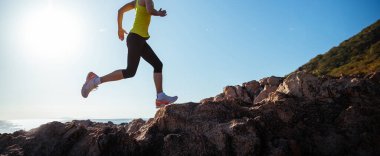 Gün doğumunda koşan kadın koşucu deniz kenarında kayalık dağlar