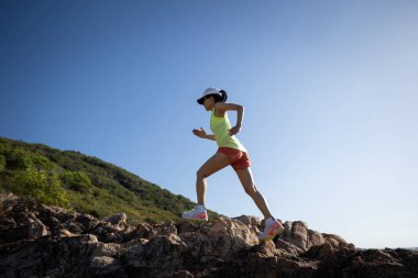 Gün doğumunda koşan kadın koşucu deniz kenarında kayalık dağlar