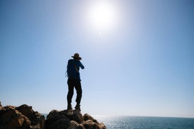 Güneş doğarken deniz kenarındaki kayalarda fotoğraf çeken kadın fotoğrafçı.