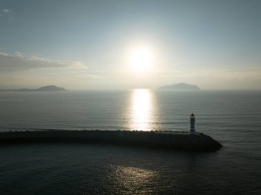 Uzun kırmızı ve beyaz çizgili deniz feneri sabah güneşinde deniz kenarında. Beyaz bulutlu mavi gökyüzü. Yaz tatili, deniz konseptinde tatil