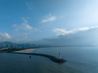 Uzun kırmızı ve beyaz çizgili deniz feneri sabah güneşinde deniz kenarında. Beyaz bulutlu mavi gökyüzü. Yaz tatili, deniz konseptinde tatil