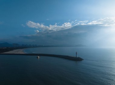 Uzun kırmızı ve beyaz çizgili deniz feneri sabah güneşinde deniz kenarında. Beyaz bulutlu mavi gökyüzü. Yaz tatili, deniz konseptinde tatil