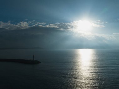 Uzun kırmızı ve beyaz çizgili deniz feneri sabah güneşinde deniz kenarında. Beyaz bulutlu mavi gökyüzü. Yaz tatili, deniz konseptinde tatil