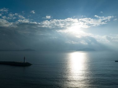 Uzun kırmızı ve beyaz çizgili deniz feneri sabah güneşinde deniz kenarında. Beyaz bulutlu mavi gökyüzü. Yaz tatili, deniz konseptinde tatil