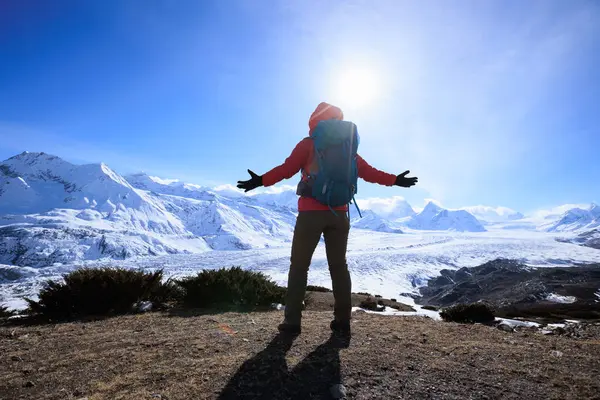 女性のハイカーは氷河の山への山頂の崖の端の表面の景色を楽しんでいます — ストック写真