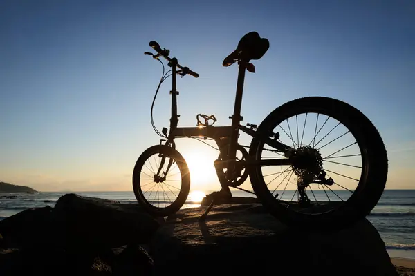日出海滨岩石上的可折叠自行车 — 图库照片