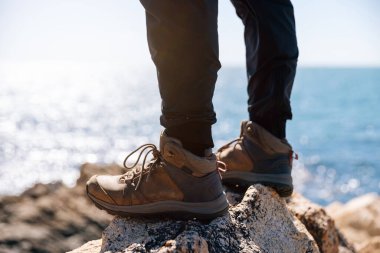 Yürüyüşçü bacakları deniz kenarındaki kayalarda duruyor.