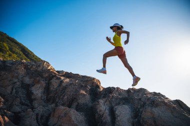 Gün doğumunda koşan kadın koşucu deniz kenarında kayalık dağlar