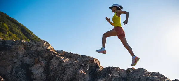 女赛跑选手在日出海滨岩石山上奔跑 — 图库照片