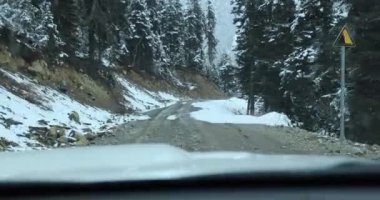 Karla kaplı yolda ve dağlarda giden araba.