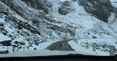 Karla kaplı yolda ve dağlarda giden araba.