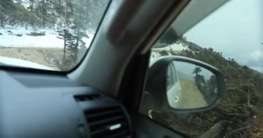 Karla kaplı yolda ve dağlarda giden araba.