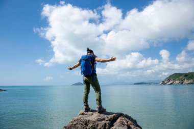 Yürüyüşçü deniz kenarındaki kayada duruyor.