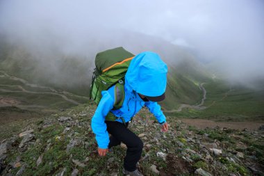 Tibet 'te dağın tepesine tırmanan bir kadın yürüyüşçü