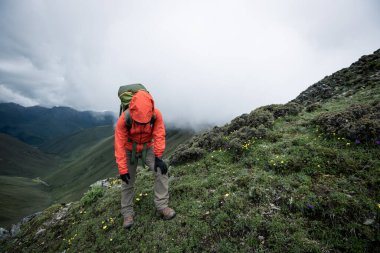 Tibet 'te dağın tepesine tırmanan bir kadın yürüyüşçü