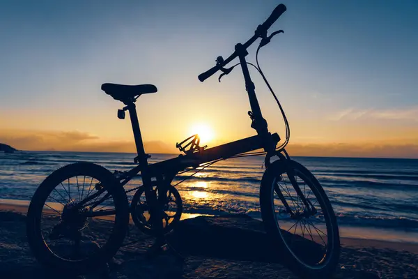 日出海滨岩石上的折叠式自行车 — 图库照片