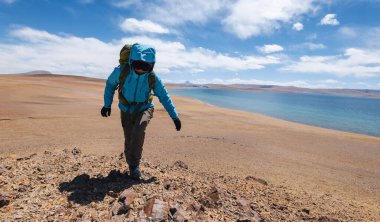 Göl kıyısındaki dağın tepesine tırmanan bir kadın yürüyüşçü.