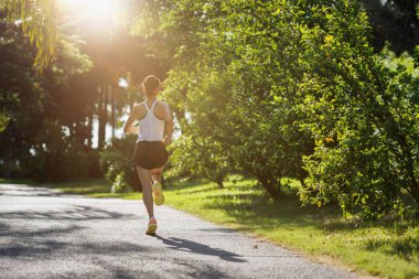 Güneşli tropik park yolunda koşan fitness kadını