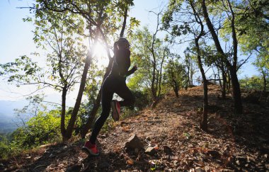 Fitness Asyalı kadın kışın gündoğumunda tropik ormanda yolda koşuyor.