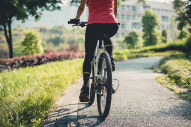Güneşli parkta dağ bisikleti süren bir kadın.