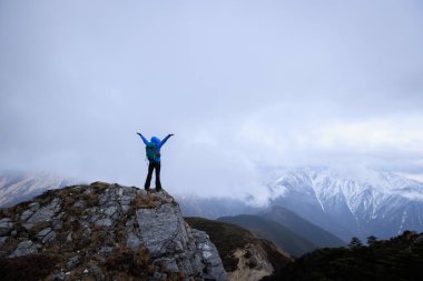 Kadın yürüyüşçü, dağın tepesindeki uçurumun keyfini çıkar. Tibet 'teki kar kaplı dağlara bak.