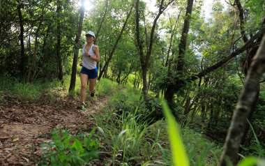 Kadın koşucu orman yolunda koşuyor.
