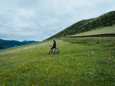 Çiçekli çayır dağında dağ bisikleti süren kadının hava manzarası.