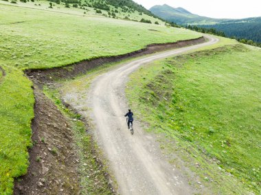 Çiçekli çayır dağ patikasında dağ bisikleti süren kadının hava manzarası.