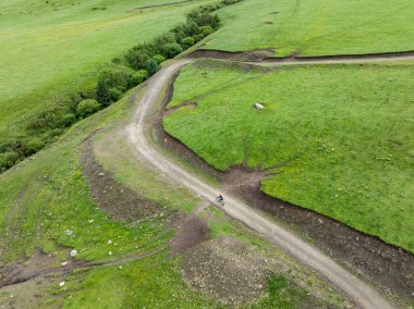 Çiçekli çayır dağ patikasında dağ bisikleti süren kadının hava manzarası.