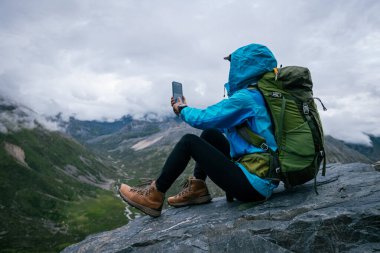 Yürüyüş yapan kadın, yüksek irtifada telefonuyla fotoğraf çekiyor.