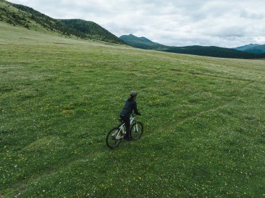 Çiçekli çayır dağ patikasında dağ bisikleti süren kadının hava manzarası.
