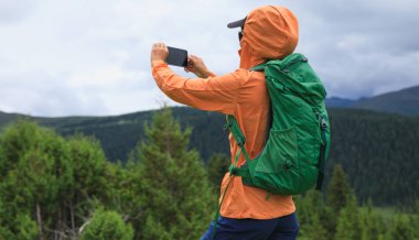 Yüksek rakımlı orman dağlarında cep telefonuyla fotoğraf çeken yürüyüşçü kadın.
