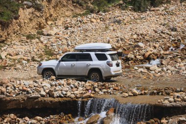 Yüksek dağlardaki kayalık nehri geçen off-road arabası sürüyorum.