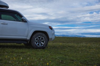 Offroad vagonu mavi gökyüzünün altında çiçek açan çayır dağında