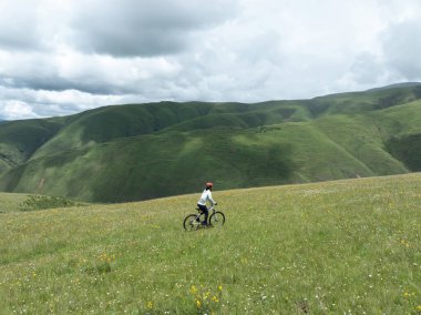 Çiçekli çayır dağ patikasında dağ bisikleti süren kadının hava manzarası.