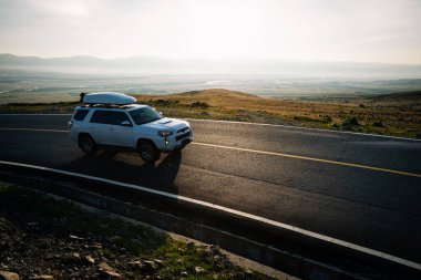 Araba güneşin doğuşunda yüksek irtifada dağın tepesinde ilerliyor.