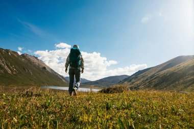 Sırt çantalı bir kadın yüksek irtifada dağ tepesinde yürüyüş yapıyor. Uzakta bir göl var.