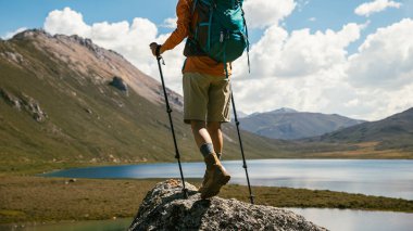 Sırt çantalı bir kadın yüksek irtifada dağ tepesinde yürüyüş yapıyor. Uzakta bir göl var.