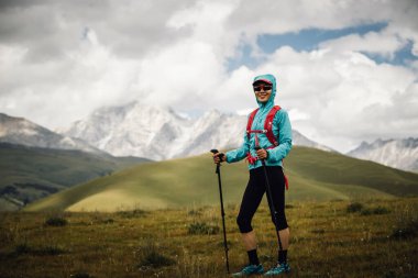 Arka planda karlı dağlarla çayırlarda koşan yorgun kadın koşucu.