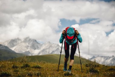 Arka planda karlı dağlarla çayırlarda koşan yorgun kadın koşucu.