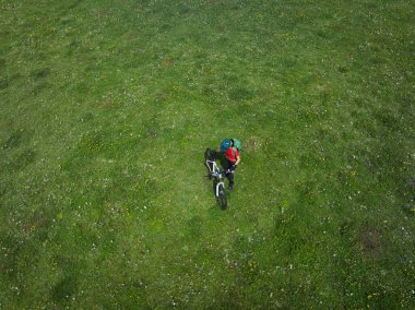 Dağ bisikleti süren bir kadının hava manzarası. Çiçekli çayırların tepesinde.
