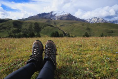 Yüksek rakımlı dağlarda yürüyüş yapan bir kadın, çimlerin üzerinde oturur.